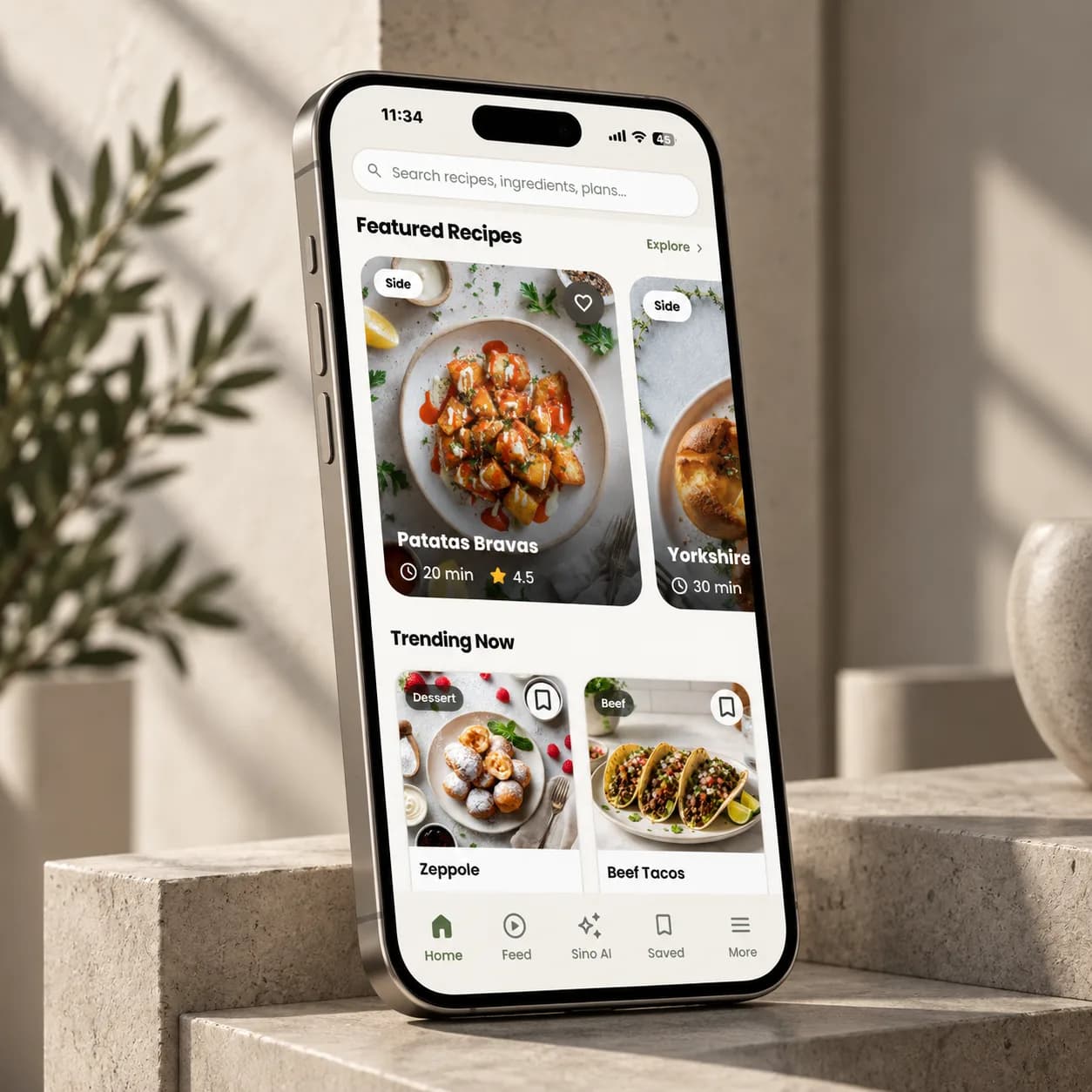 Sino Recipes, the AI kitchen assistant we developed, on a phone propped against a stone plinth, showing the home feed of featured and trending recipes